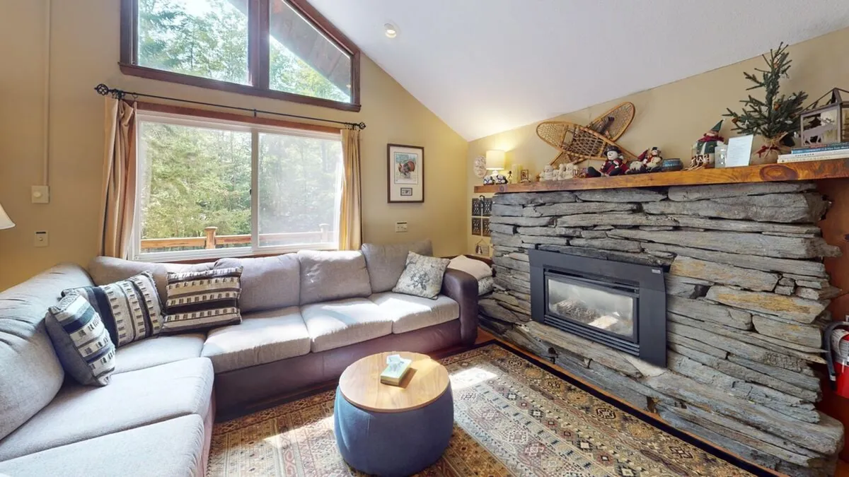 This image showcases a cozy living area anchored by a stone fireplace, with a comfortable couch and large windows that flood the space with natural light. Decorative items on shelves add a touch of homeliness, while the overall atmosphere exudes warmth and relaxation—perfect for gatherings after a day outdoors.
