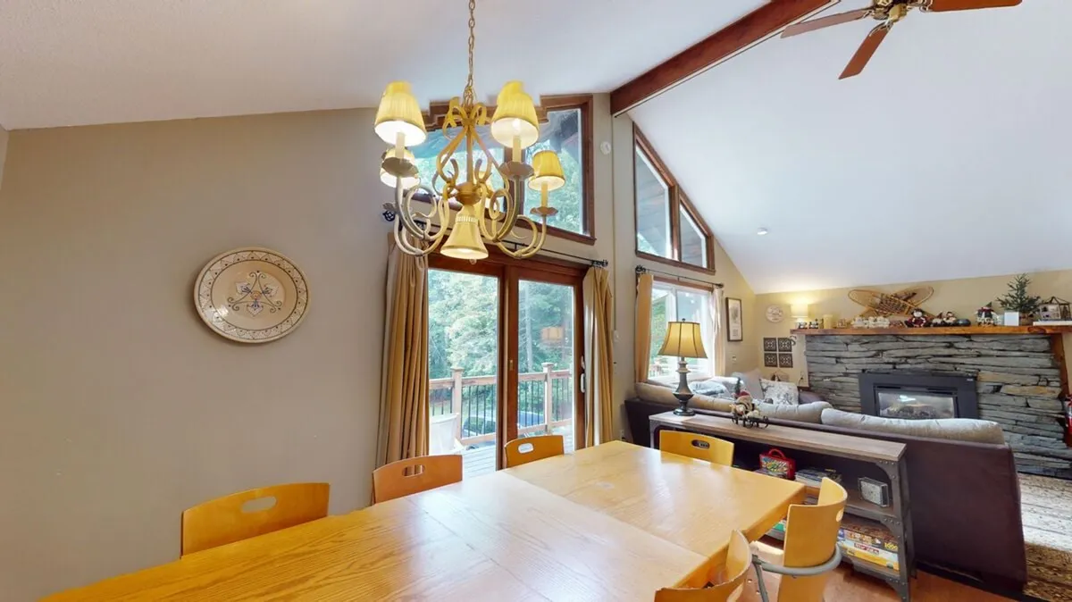 A warmly lit interior diner with a prominent dining table under a chandelier, flanked by large windows and a striking stone fireplace. The ambiance invites group dinners, reading by the fire, and celebrations, underlining the cozy, inviting feel described in the section.
