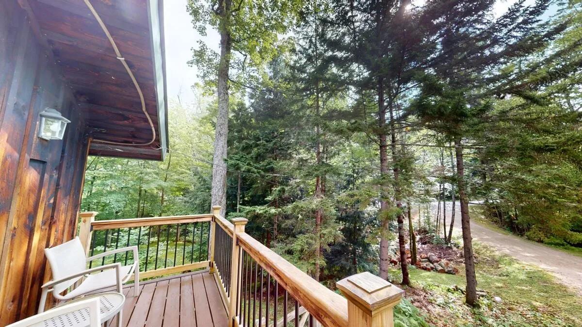 This exterior shot highlights a spacious wooden deck surrounded by trees and a pathway, offering an immersive view of the serene, forested setting. The peaceful outdoor scene suggests the proximity to nature and opportunities for morning coffee or evening stargazing.