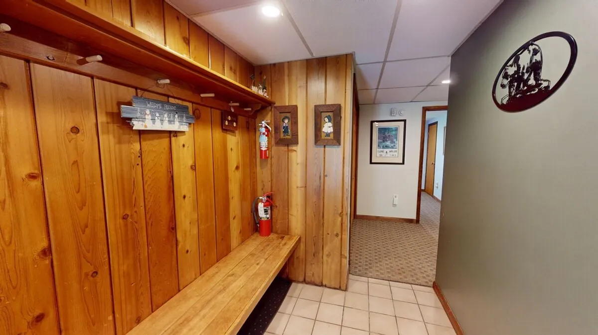 A cozy entry area featuring a wooden bench, wall hangings, and visible fire extinguishers. The space is practical and welcoming, suggesting a spot where guests can prepare for or return from outdoor adventures. The bench provides a convenient place to put on or store boots and gear.