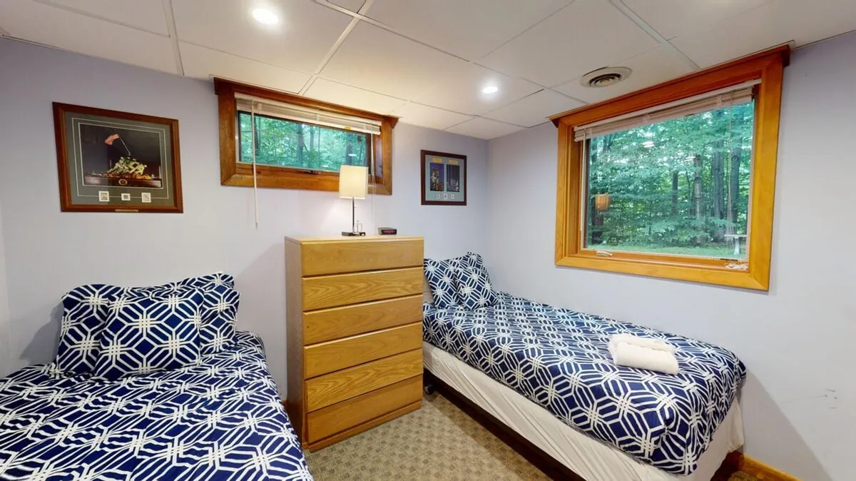 A cozy bedroom featuring two twin beds with patterned comforters, a wooden dresser, and a window providing views of the surrounding trees. The mood is tranquil and inviting, ideal for relaxation and enjoying quiet moments after a day of adventure.